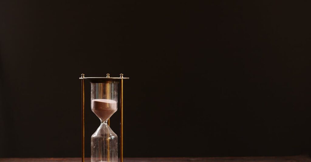 A classic hourglass with sand trickling down, symbolizing the passage of time, against a dark background.