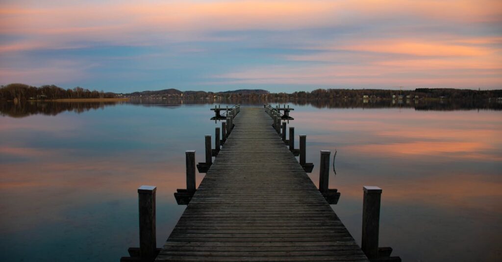 A tranquil lake with a wooden jetty under a colorful sunset sky, reflecting calm waters.