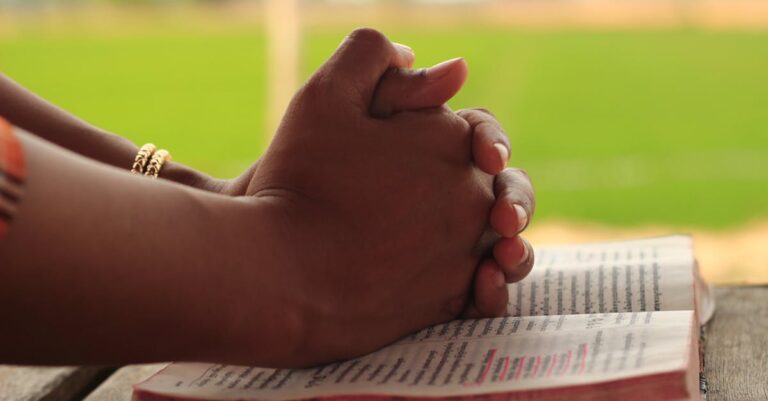 Close-up of hands clasped in prayer over an open Bible, symbolizing faith and devotion.