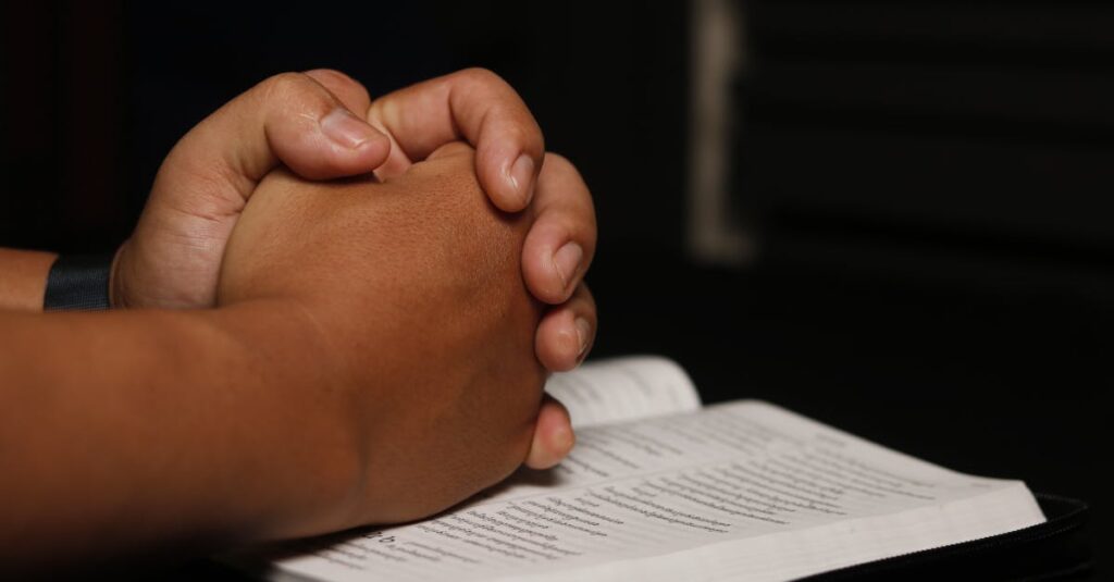Hands clasped in prayer over an open book, symbolizing spirituality.
