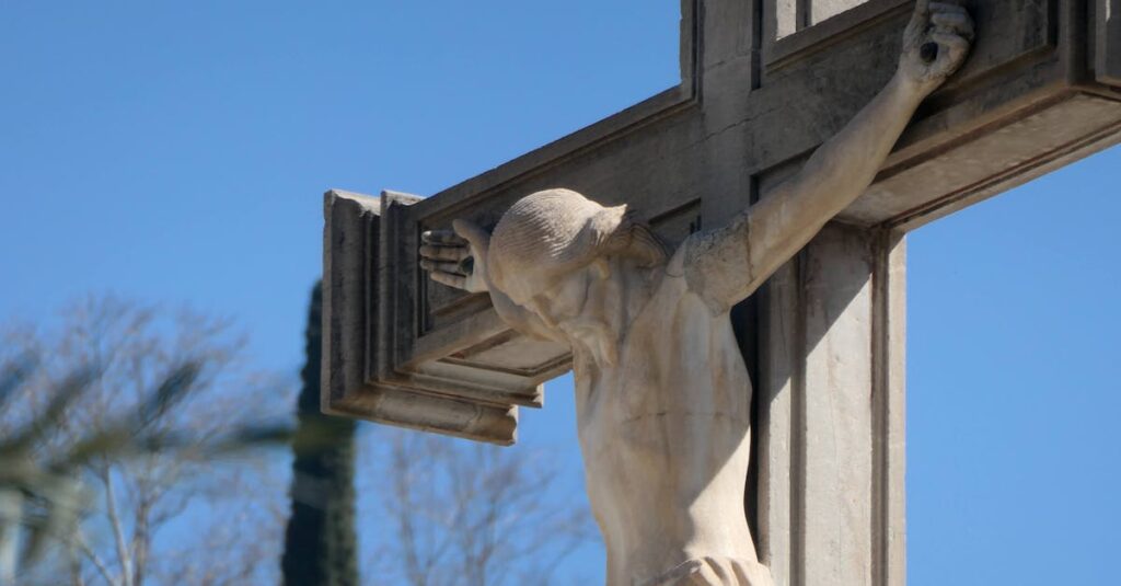 Close-up of a stone crucifix with Jesus statue against a vibrant blue sky, symbolizing faith.