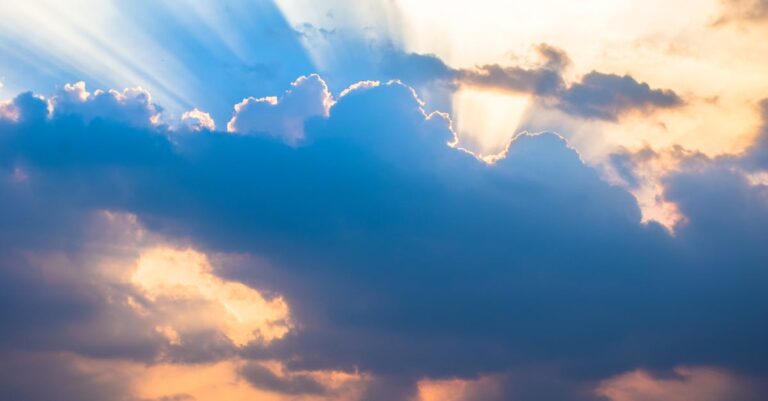 A dramatic sky with sunbeams piercing through clouds during a vibrant sunset.