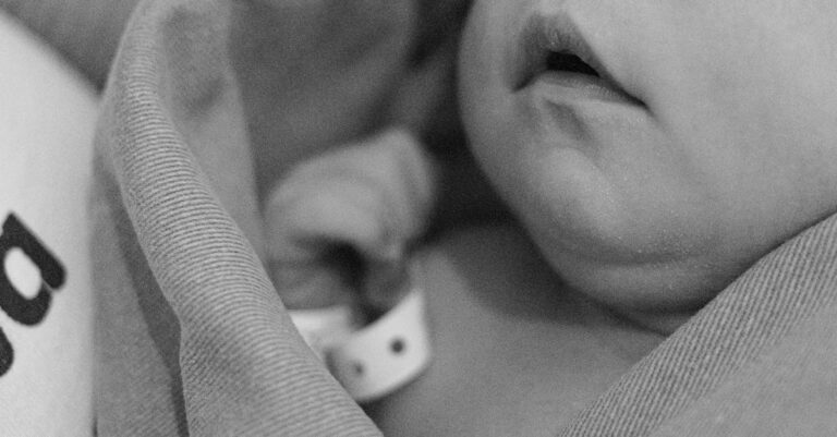 A close-up black and white photo of a newborn baby swaddled in a blanket.