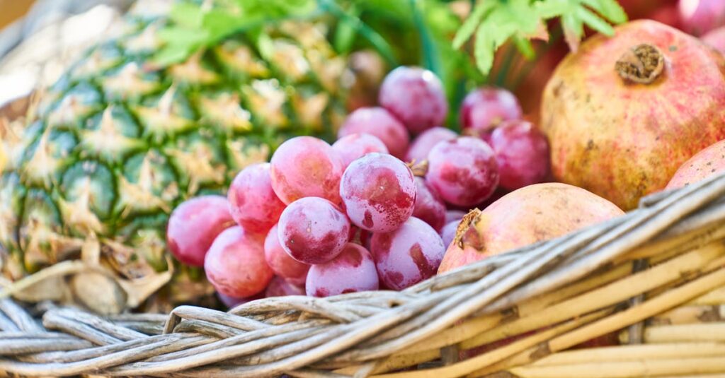 A colorful mix of fresh fruits including grapes, pineapple, and pomegranates in a wicker basket.