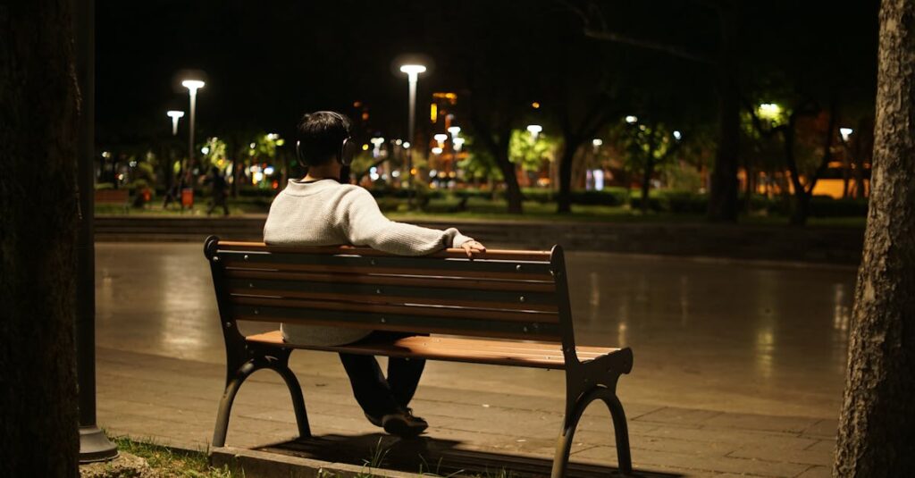 pexels-photo-31724740-31724740 Solitary figure listening to music on a park bench under night streetlights, urban solitude.