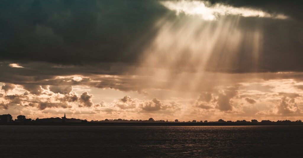 Sunbeams illuminate a serene landscape beneath dark storm clouds over a calm sea.