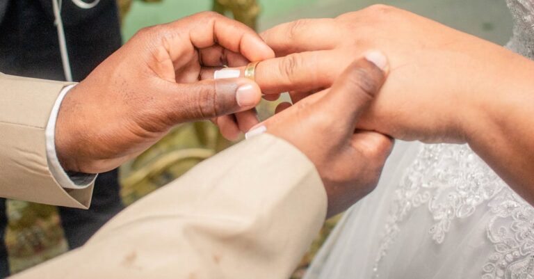 A close-up captures a groom placing a wedding ring on the bride's finger during their ceremony.