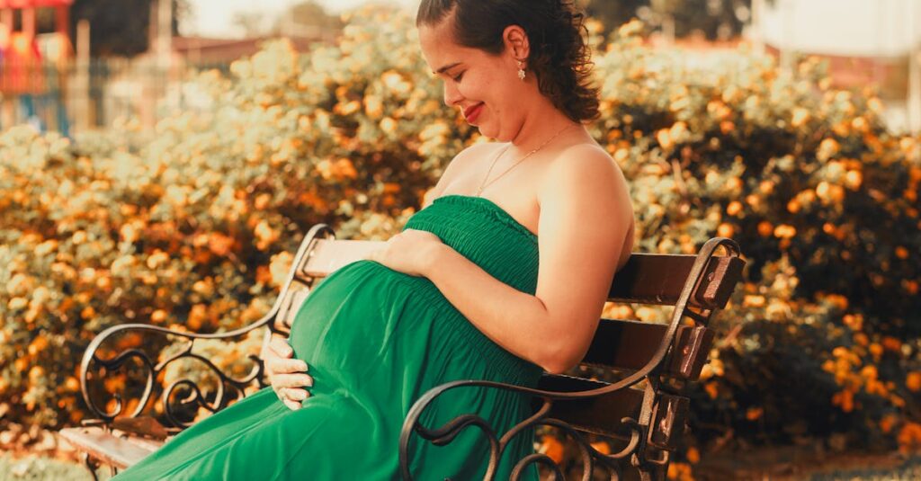 A pregnant woman in a green dress sits on a park bench, radiating joy.