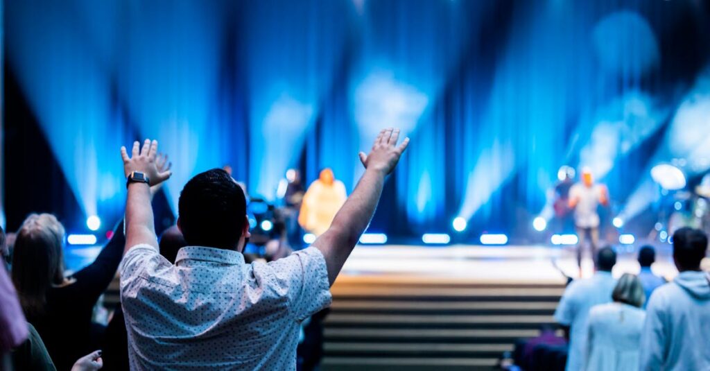 Group of people attending a lively worship service in a modern auditorium setting.