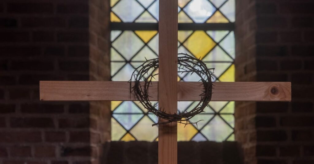 A wooden cross with a crown of thorns against a stained glass window in a church setting.