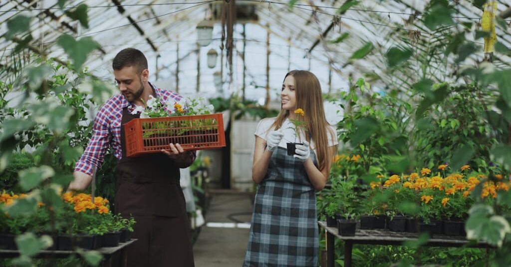 Two gardeners tending plants in a vibrant greenhouse filled with flowers.