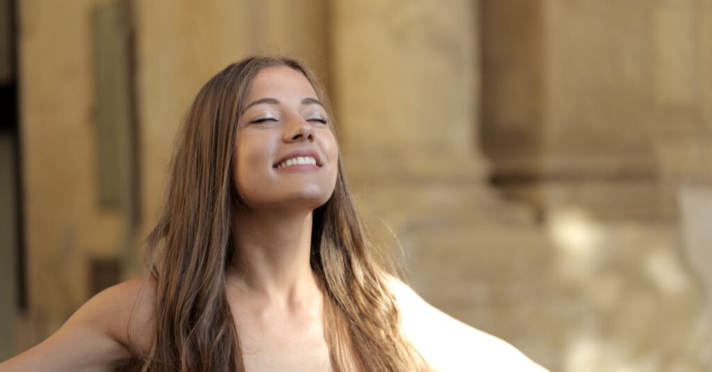 Smiling woman with closed eyes embracing the outdoors in warm sunlight.