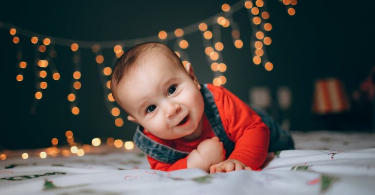 Adorable little boy lying on bed against bright Christmas lights in cozy room