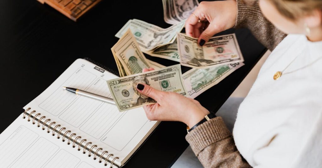 Woman organizing finances, counting dollar bills at desk with open notebook.