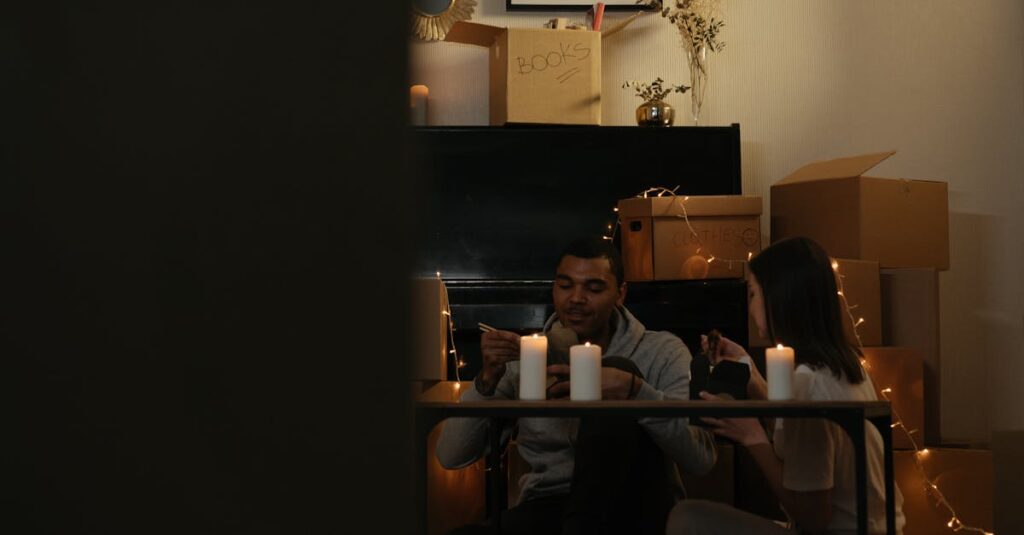 Couple enjoying a meal by candlelight surrounded by moving boxes in a cozy home setting.