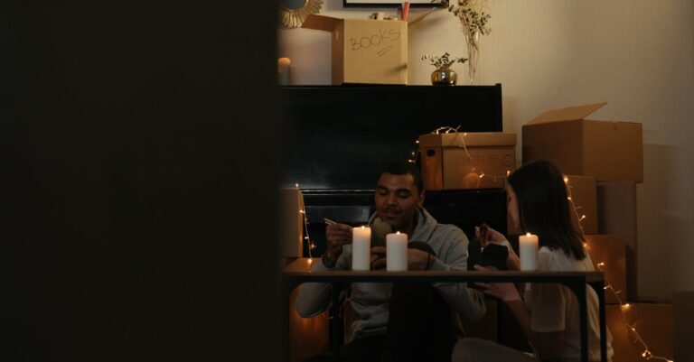 Couple enjoying a meal by candlelight surrounded by moving boxes in a cozy home setting.