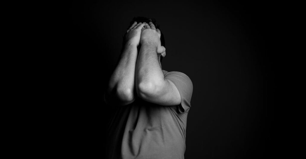 A man in a t-shirt covers his face with both hands, conveying deep emotion and distress.
