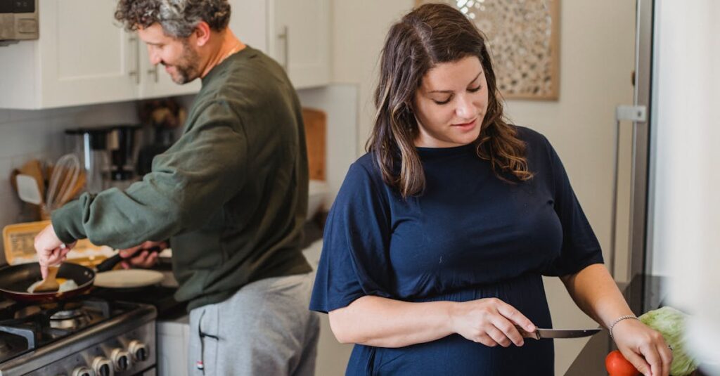 Adult pregnant woman in casual dress cutting vegetables while husband cooking meal on heater in contemporary light kitchen