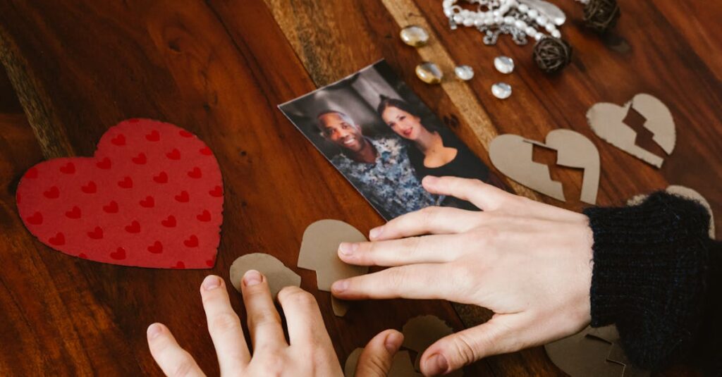 Close-up of hands arranging broken hearts near a couple's photo on a wooden table.