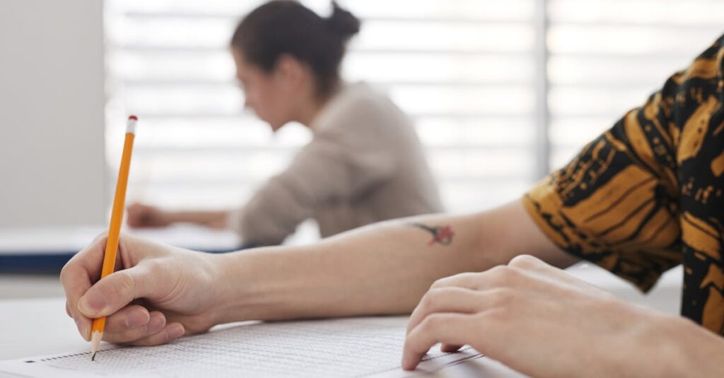 Close-up of student's hands writing on exam sheet, indoors with blurred background.