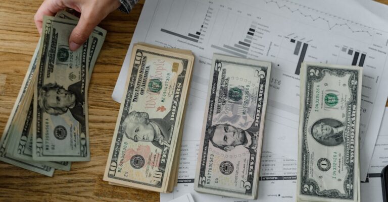 Person holds US dollars over financial papers, showing income or budget analysis.