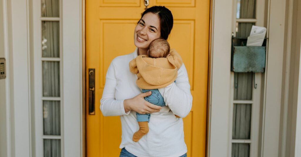 A joyful mother embraces her baby in front of a bright yellow door, symbolizing motherhood and warmth.