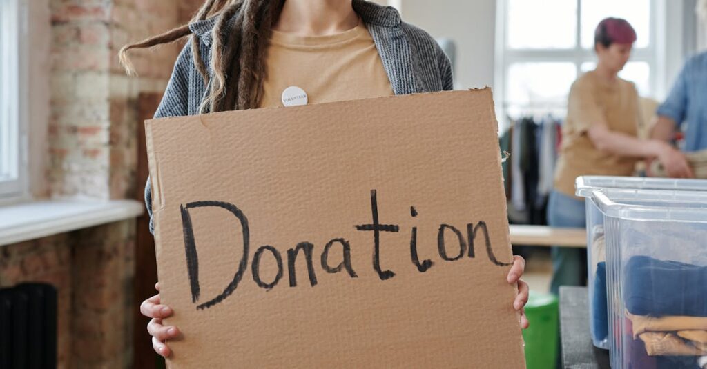 Volunteer holding a cardboard donation sign in a community center with clothing and supplies.