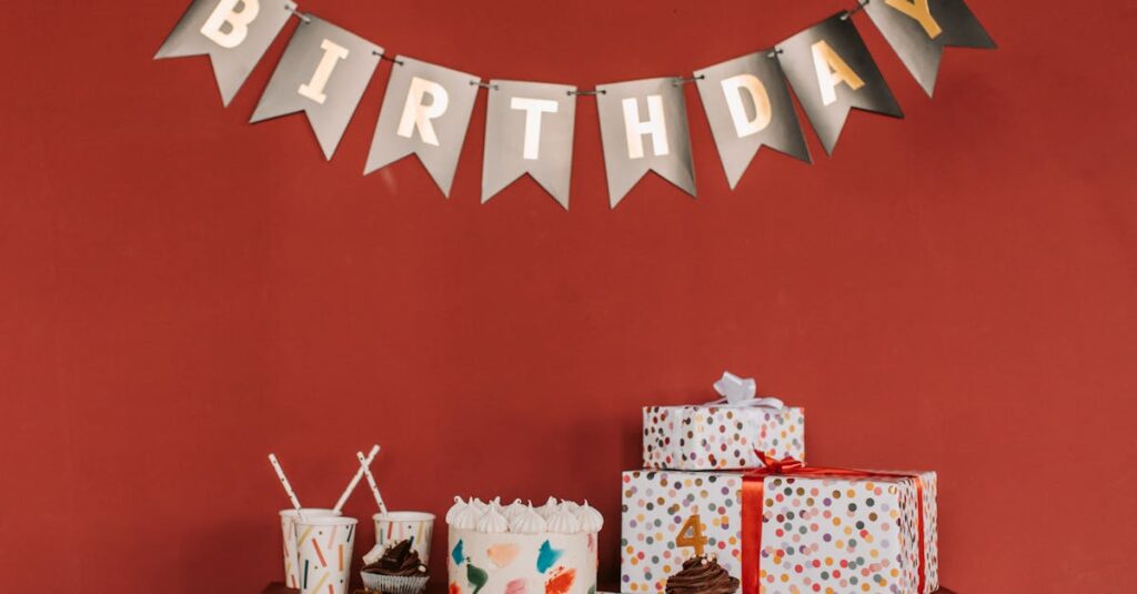 Festive birthday scene with cake, cupcakes, gifts, and decorations against red wall.