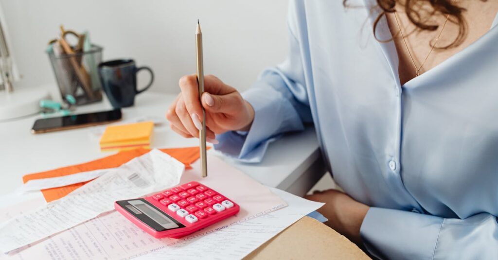 A woman is calculating expenses using a calculator and papers at her desk.