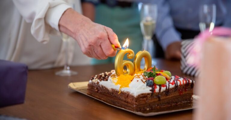 Hand lighting candles on birthday cake with number 60 on it at a celebration.