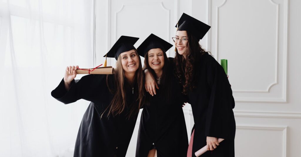 Three smiling graduates in caps and gowns celebrating indoors together.