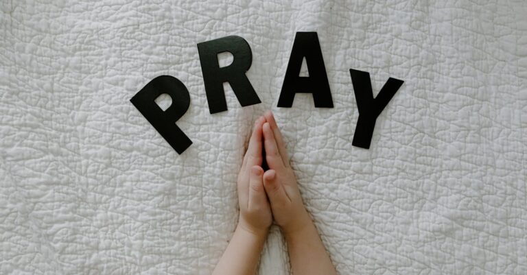 Close-up of hands in prayer on white quilted fabric with PRAY letters.