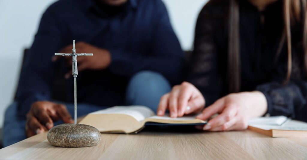 Two individuals study the Bible with a cross on the table, symbolizing faith and devotion.