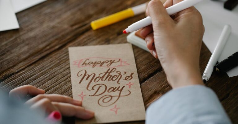 Close-up of a person designing a Mother's Day card with calligraphy on wooden table.