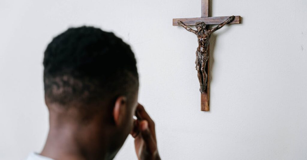 A person praying before a wooden crucifix on a plain wall, symbolizing faith and devotion.