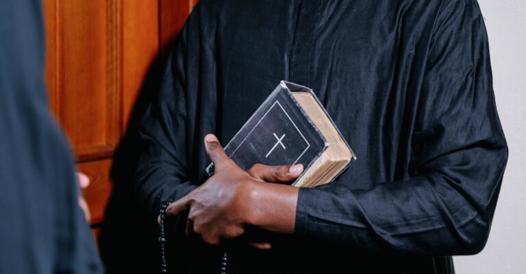 Close-up of a priest holding a Bible and rosary beads, symbolizing faith and spirituality.