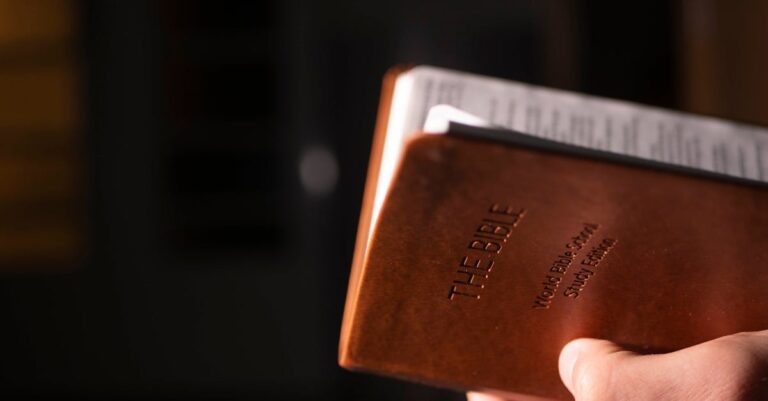 Close-up view of a hand holding a leather-bound Bible, featuring selective focus.