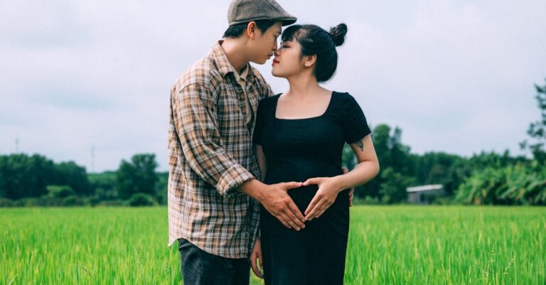 Pregnant couple embracing in a lush green field, symbolizing love and togetherness.