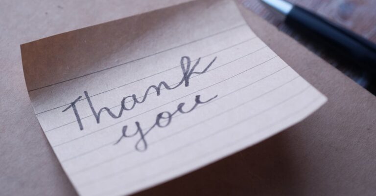 Close-up of a handwritten thank you note on brown paper with a pen nearby.
