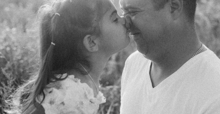 Black and white photo of a loving father and daughter sharing a tender moment outdoors.
