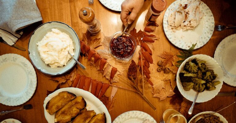 Overhead view of a traditional Thanksgiving dinner table with various dishes and autumn leaves.