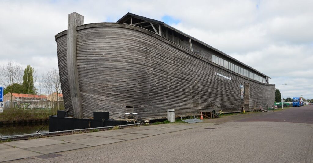 pexels-photo-31918251-31918251 Large wooden structure by canal, resembling a historical ark on a cloudy day.