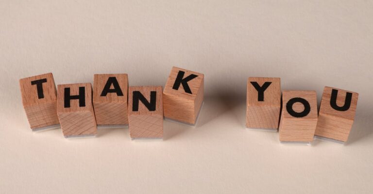 Wooden blocks spell 'THANK YOU' on a soft beige background, expressing gratitude.