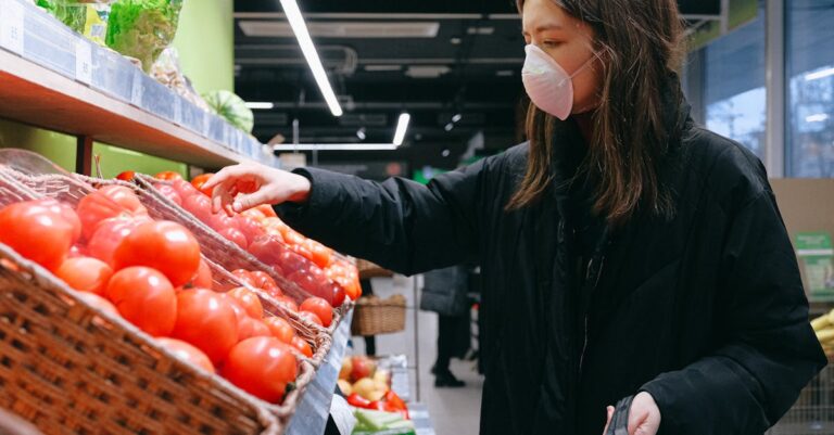 A woman wearing a face mask chooses fresh tomatoes in a supermarket.