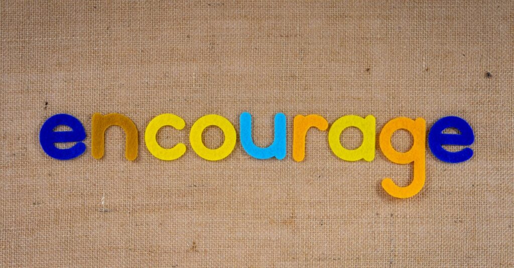 The word 'encourage' in colorful letters on a brown burlap texture, conveying positivity and motivation.
