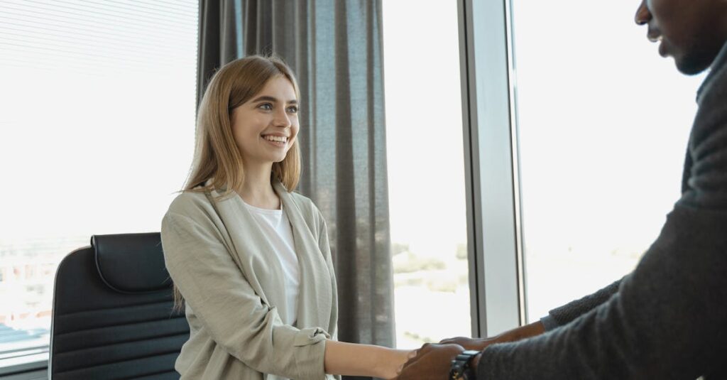 Woman smiling and shaking hands at a business office, signaling a successful job interview.