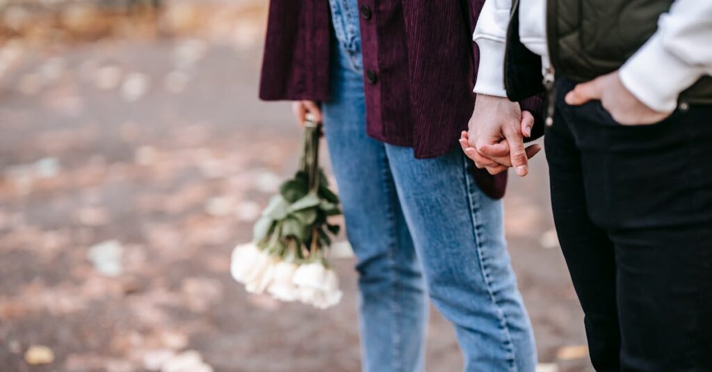 Crop anonymous couple with fresh white roses holding hands on blurred background of park