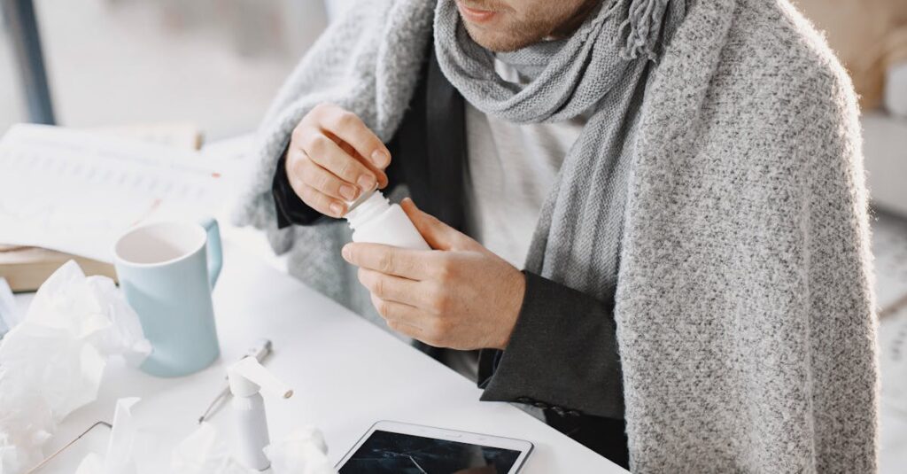 Adult male in scarf taking medicine at a desk with tissues and tablet, feeling unwell.