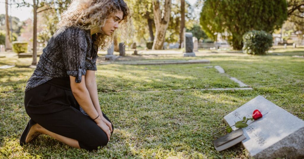 A woman kneeling by a grave in a sunlit cemetery, expressing grief and remembrance.