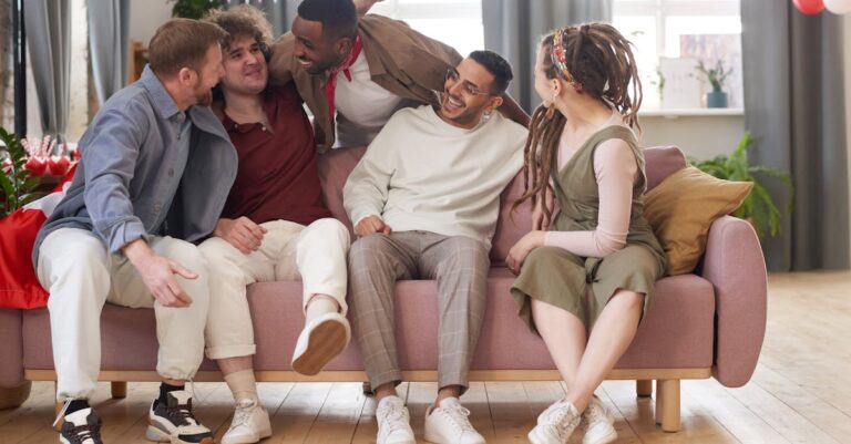Five diverse friends laughing and bonding on a couch in a cozy indoor setting.